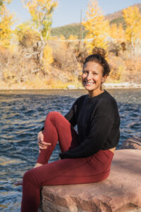 Photo of Dana Wood sitting on a rock beside a river