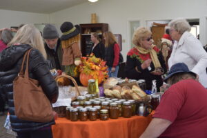 Photo of a group of people standing around a table with jarred food